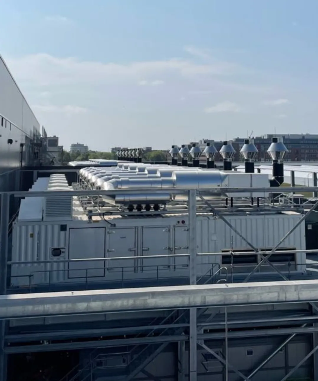 Rooftop view of a data center with rows of standby generators, exhaust ducting and stack outlets along the building edge