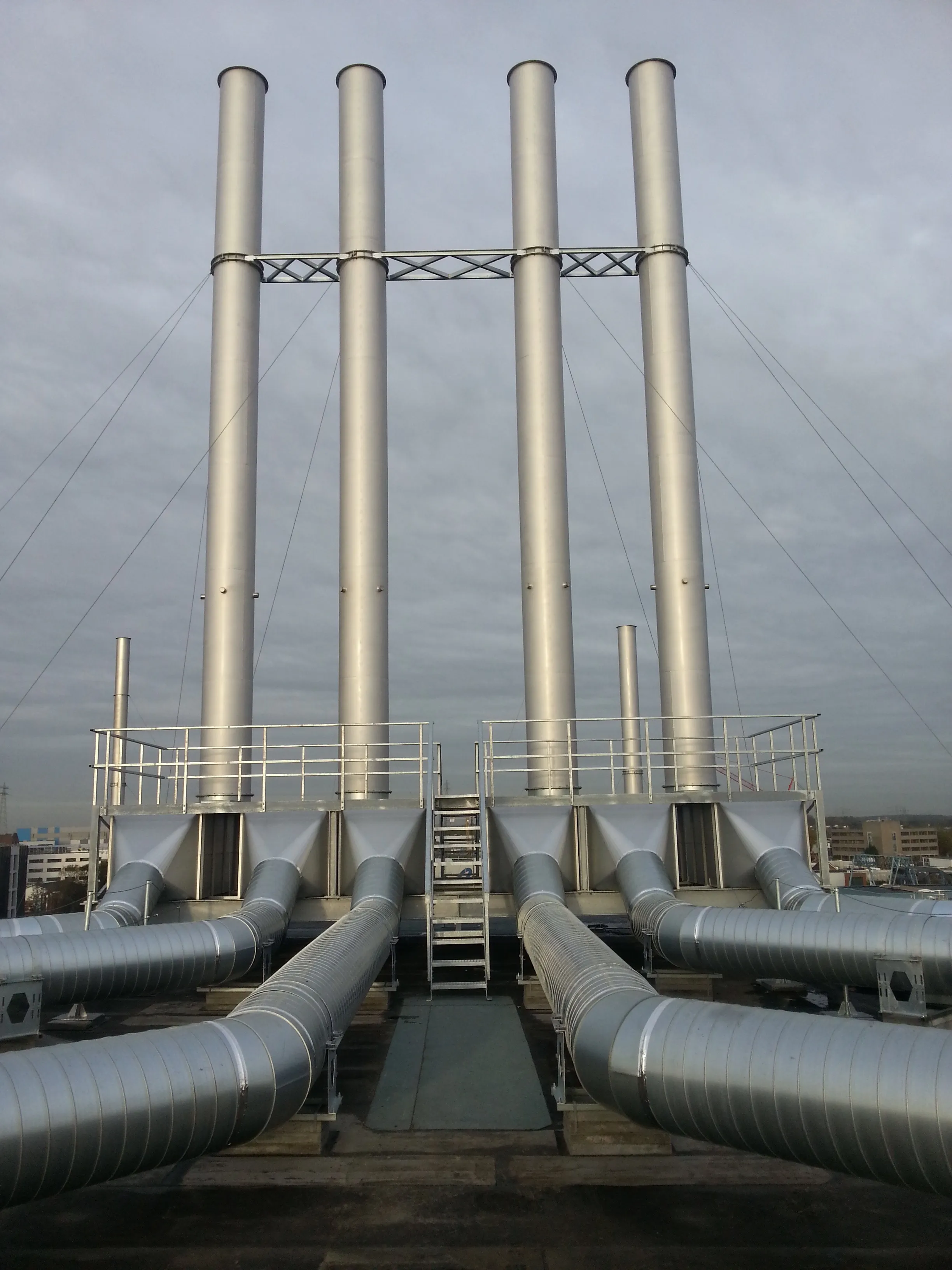 Four freestanding Axces exhaust stacks above a manifold of cross-braced ducting on an industrial rooftop