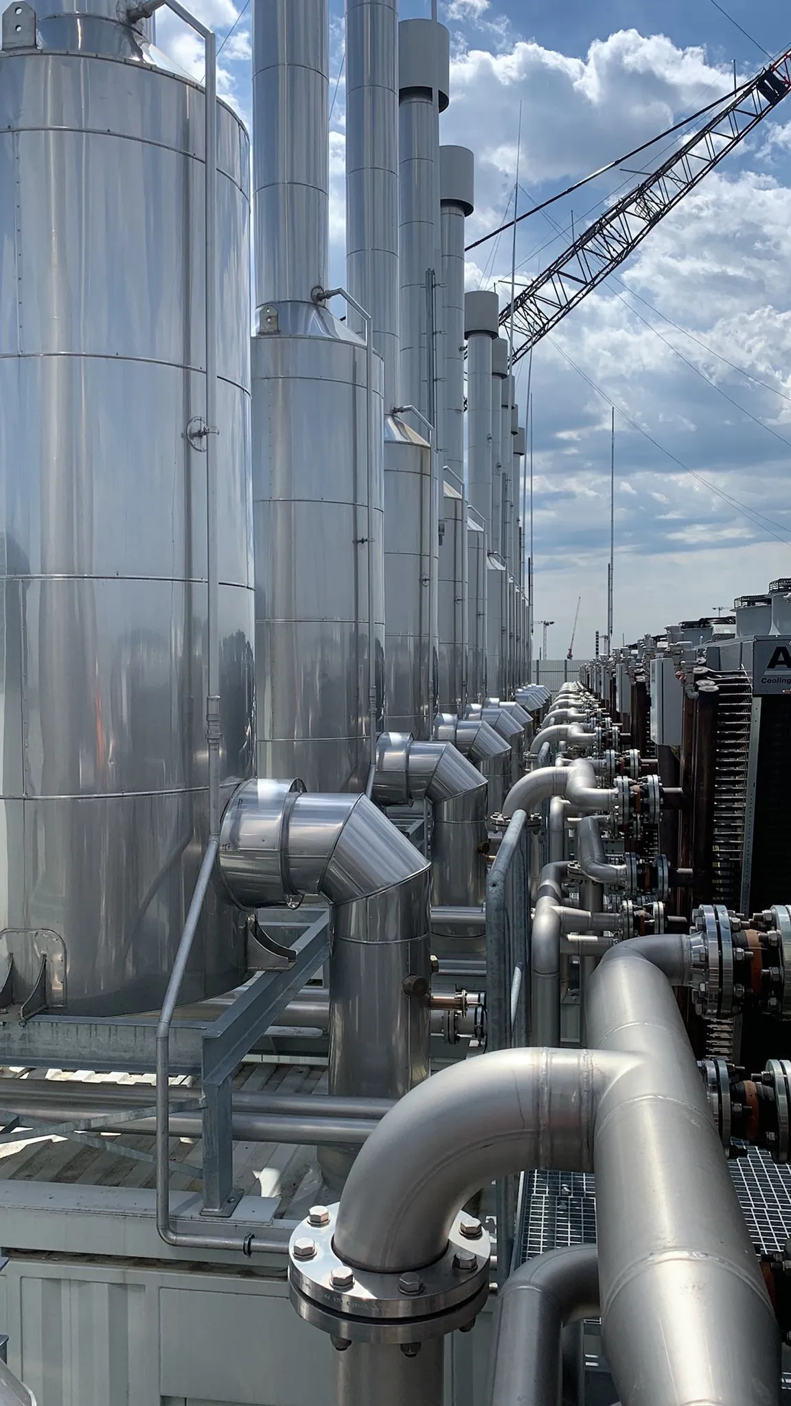 Row of stainless-steel exhaust silencers and ducting along the deck of an Axces power generation installation