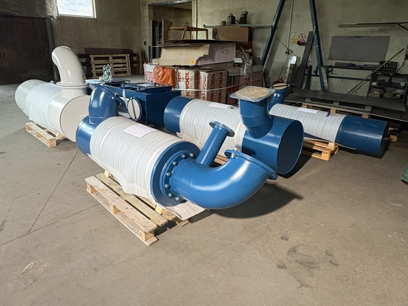 Blue blower discharge and inlet silencers with flanged elbows on pallets, ready for dispatch
